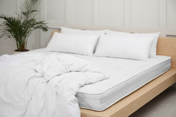Wooden bed with soft white mattress, blanket and pillows indoors