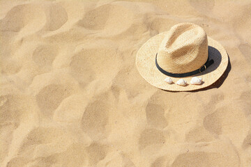 Fototapeta na wymiar Straw hat with seashells on sandy beach, space for text