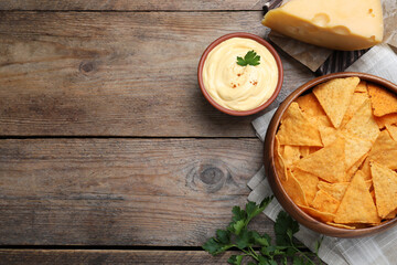 Delicious nachos and cheese sauce with parsley on wooden table, flat lay. Space for text