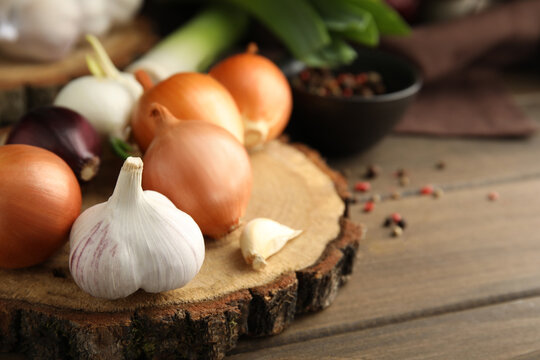 Fresh onion bulbs, leek and garlic on wooden table, closeup. Space for text
