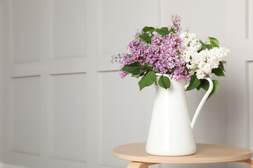 Beautiful lilac flowers in vase on wooden table near white wall. Space for text