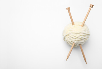 Soft yarn with knitting needles on white background, top view