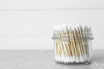 Fototapeta na wymiar Many cotton buds in glass jar on light grey marble table, space for text
