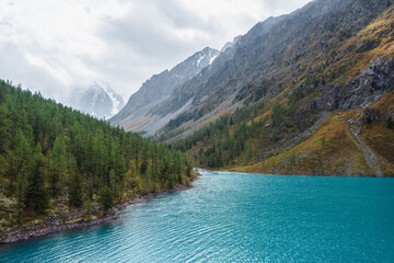 Shiny ripples on turquoise alpine lake against snowy mountain range during rain in changeable...