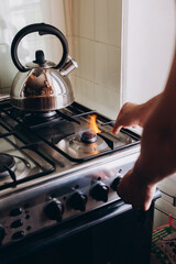 A man's hand with a match lights a gas burner or a gas stove in the kitchen