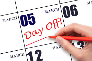5th day of March. Hand writing text DAY OFF and drawing a line on calendar date 5 March. Vacation...