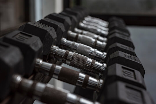 A rack of hex dumbbells at a gym or fitness club. Workout and pyramid training or running the rack for serious bodybuilding concept. - Powered by Adobe
