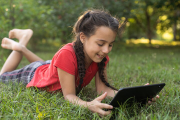 Girl on the grass with a tablet chat in her hands in the garden