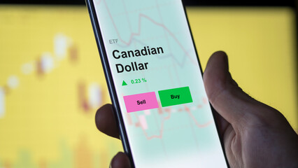An investor's analyzing the canadian dollar cad etf fund on a screen. A phone shows the prices of...
