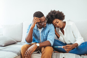 Upset man and woman sitting on couch apart, holding pregnancy test, unintended pregnancy concept....