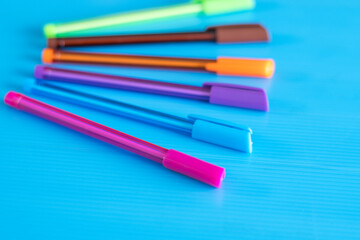 Fototapeta premium Side view of selective focus shot of color pens lying on blue background. 