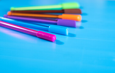 Side view of selective focus shot of color pens lying on blue background. 