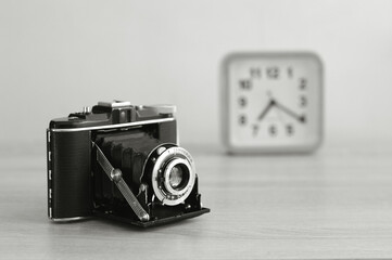 Vintage analog medium format film camera and a clock in black and white. Old film camera with bellows.