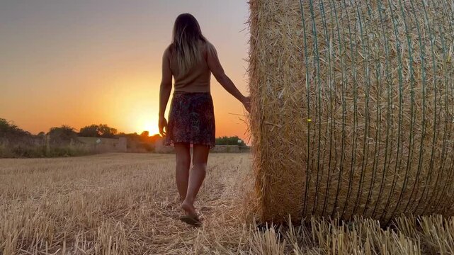 Mujer viendo atardecer en verano en el campo  andando al lado de una bala de paja