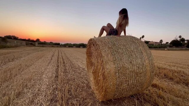 Chica viendo atardecer en verano subida sobre una bala de paja
