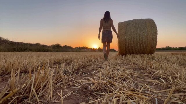 Mujer viendo atardecer en verano en el campo  andando al lado de una bala de paja