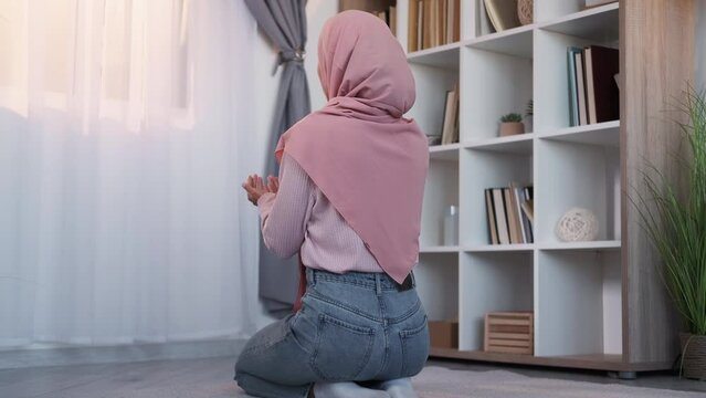 Islamic prayer. Muslim faith. Ramadan praying. Back view of faithful woman in hijab reading Holy Koran praise to Allah at window on floor at home.