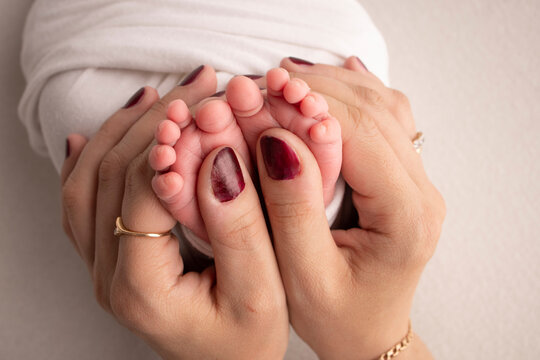 The palms of the parents. A father and mother hold the feet of a newborn child in a white blanket on a white background.. The feet of a newborn in the hands of parents. Photo of foot, heels and toes
