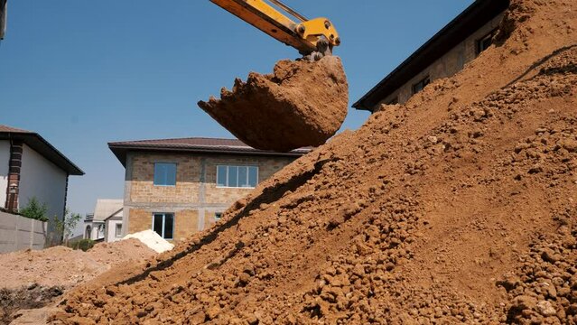 An excavator unloads clay from a bucket, creating a large mountain of soil
