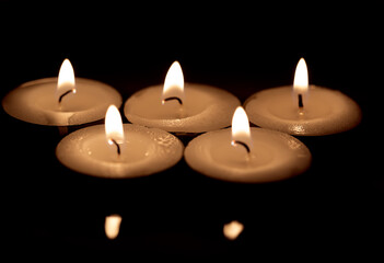 Burning tea candles isolated on dark surface background.