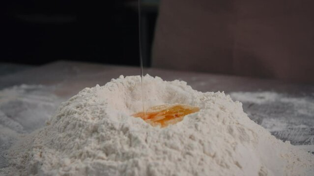 The baker puts the egg into the flour close-up.