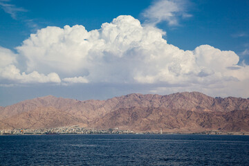 Beautiful desert mountains of Jordan against the backdrop of large white clouds. A beautiful city...