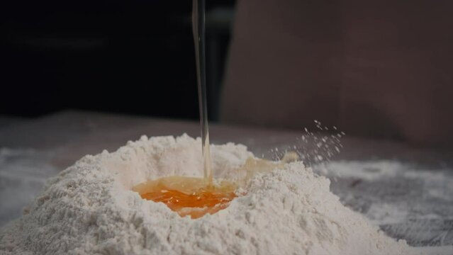 The baker puts the egg into the flour close-up.