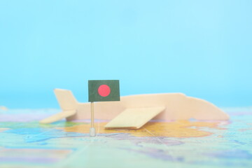 Selective focus of Bangladesh flag in blurry world map and wooden airplane model. Bangladesh as travel and tourism destination concept.