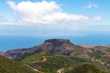 Fototapeta premium Panoramic view on massive volcanic plug Fortaleza de Chipude overlooking western coast of La Gomera, Canary Islands, Spain, Europe. Atlantic Ocean in background. Hilly mountain road to Valle Gran Rey