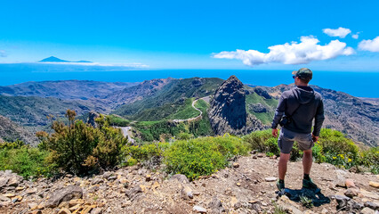 Man with scenic view on mountain road next to volcanic rock formation Roque de Agando in Garajonay National Park on La Gomera, Canary Islands, Spain, Europe. Seen from lookout Mirador Morro de Agando