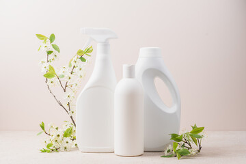 Set of white bottles with cleaning products and blossoming tree branches on beige background. Cleaning service concept.