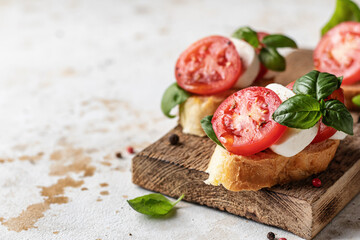 Caprese bruschetta with tomatoes, mozzarella and basil on wooden board. Text space