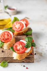 Italian bruschetta with tomatoes, mozzarella and basil on rustic wooden board with ingredients. Copy space