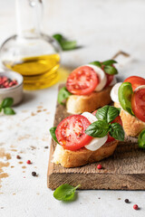 Italian bruschetta with tomatoes, mozzarella and basil on rustic wooden board with ingredients. Copy space