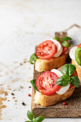Caprese bruschetta with tomatoes, mozzarella and basil on wooden board. Text space