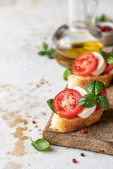 Italian bruschetta with tomatoes, mozzarella and basil on rustic wooden board with ingredients. Copy space