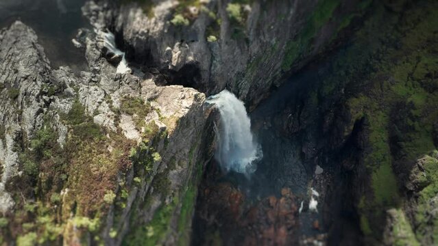 Aerial view of the waterfall cascading through the deep rocky canyon. Water dust rising high in the air. Slow-motion.