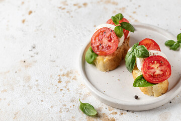 Italian bruschetta with tomatoes, mozzarella and basil on white plate with text space