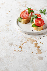 Fototapeta na wymiar Italian bruschetta with tomatoes, mozzarella and basil on white plate with text space