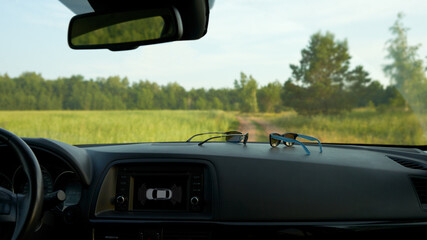 Traveling by car with a child. Dashboard with children's and adult sunglasses. Behind the windshield is a road and a green field.