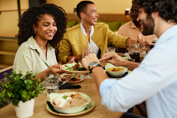 A small interracial group of friends is sitting in a restaurant and having dinner. - 518529692
