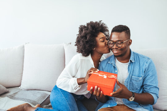 Happy young diverse couple celebrating Valentine's day together at home, with boyfriend buying a Valentine's present to his girlfriend, making her feel loved and special