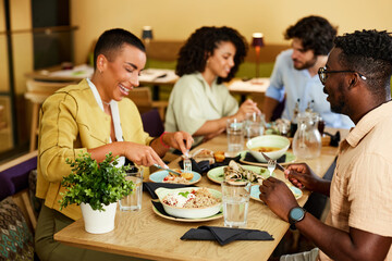 Multicultural friends are sitting in a restaurant, eating food and talking.