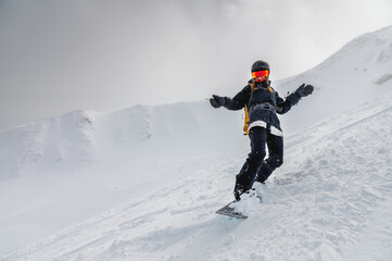 Fototapeta na wymiar Young stylish girl or woman in motion snowboarding in the mountains