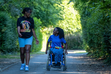 Teenage girl (16-17) in wheelchair with friend walking in park