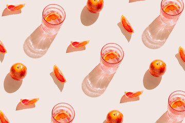Creative pattern made of bloody orange and glass of fresh cocktail or lemonade on pastel beige backgound. Summer refreshment concept. Sunlit flat lay. Minimal style. Top view