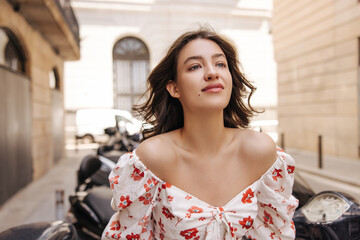 Calm young caucasian girl looks into distance enjoying spending time outdoors. In summer, brunette...
