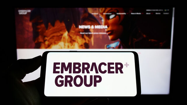 Stuttgart, Germany - 07-16-2022: Person holding smartphone with logo of Swedish media company Embracer Group AB on screen in front of website. Focus on phone display.