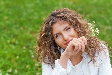 Beautiful woman with curly hair in field with dandelions in her hand.