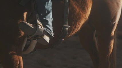 Boot in stirrup. Cowboy boot in saddle. Boots and spurs close up. Barrel racing on a horse. Riding on a horse in arena. Western clothing and a horse.